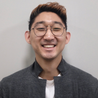 Man wearing glasses and a gray jacket against a plain background