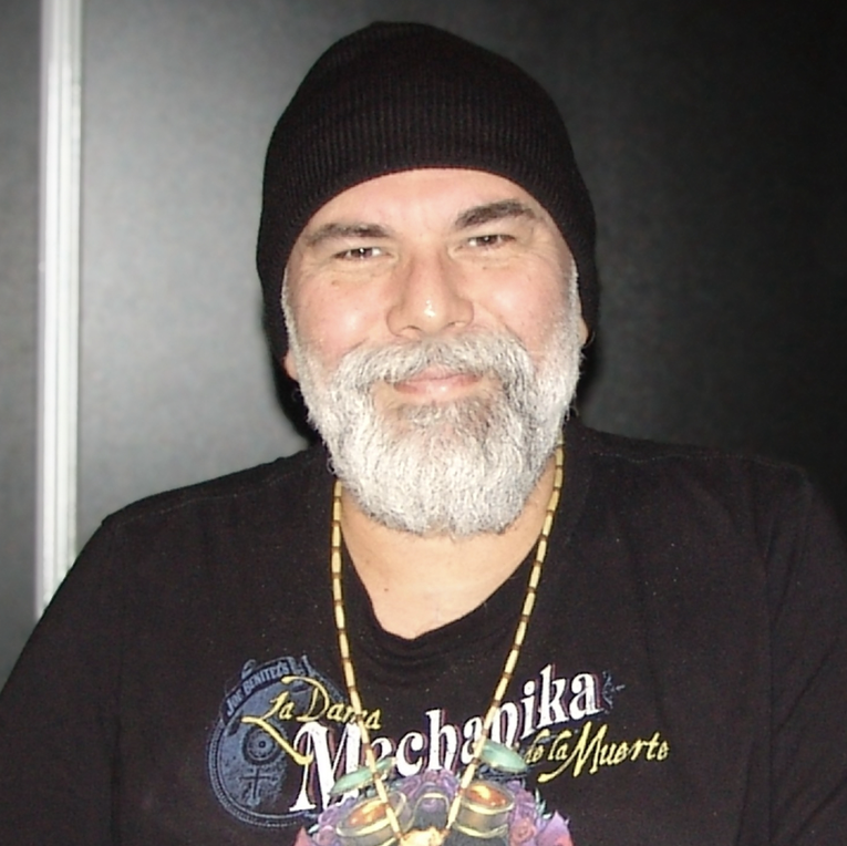 Man wearing a black beanie and black shirt with visible text, against a dark background
