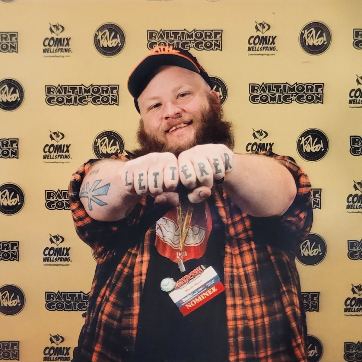 Person with tattoos on arms posing in front of a Baltimore Comic-Con backdrop