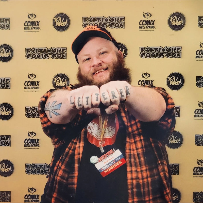 Person with tattoos on arms posing in front of a Baltimore Comic-Con backdrop